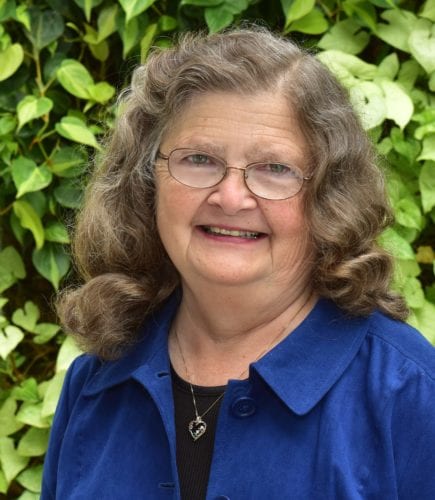 A smiling woman with curly hair wearing a blue jacket.