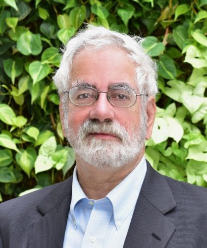 Portrait of an older man with white hair and glasses outdoors.