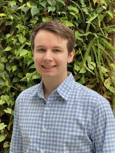 Young man smiling in a checkered shirt outdoors.
