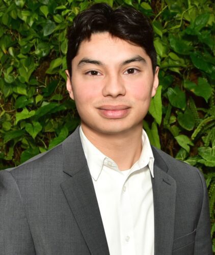 Young man in a gray suit with green foliage background.