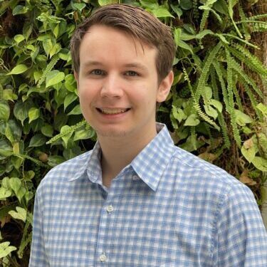Young man smiling in a checkered shirt outdoors.