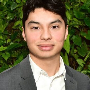 Young man in a gray suit with green foliage background.