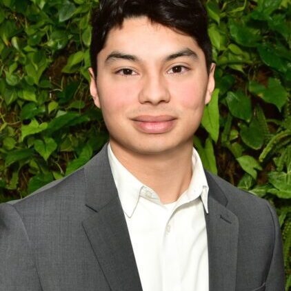 Young man in a gray suit with green foliage background.