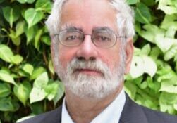 Portrait of an older man with white hair and glasses outdoors.