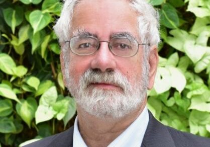 Portrait of an older man with white hair and glasses outdoors.
