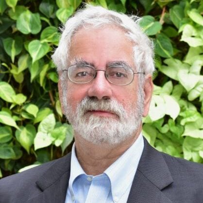 Portrait of an older man with white hair and glasses outdoors.