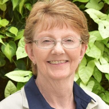 Smiling elderly woman with glasses outdoors.