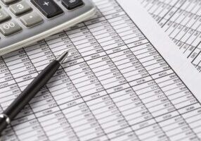 A calculator, a pen, and a financial spreadsheet with columns of numbers on a desk.
