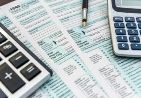 A close-up of U.S. 1040 tax forms with two calculators and a pen.